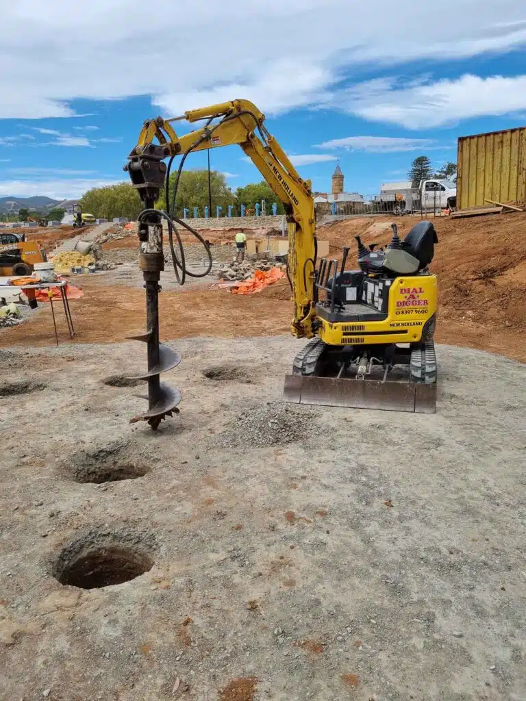 Mini excavator with an auger drilling a row of post holes
