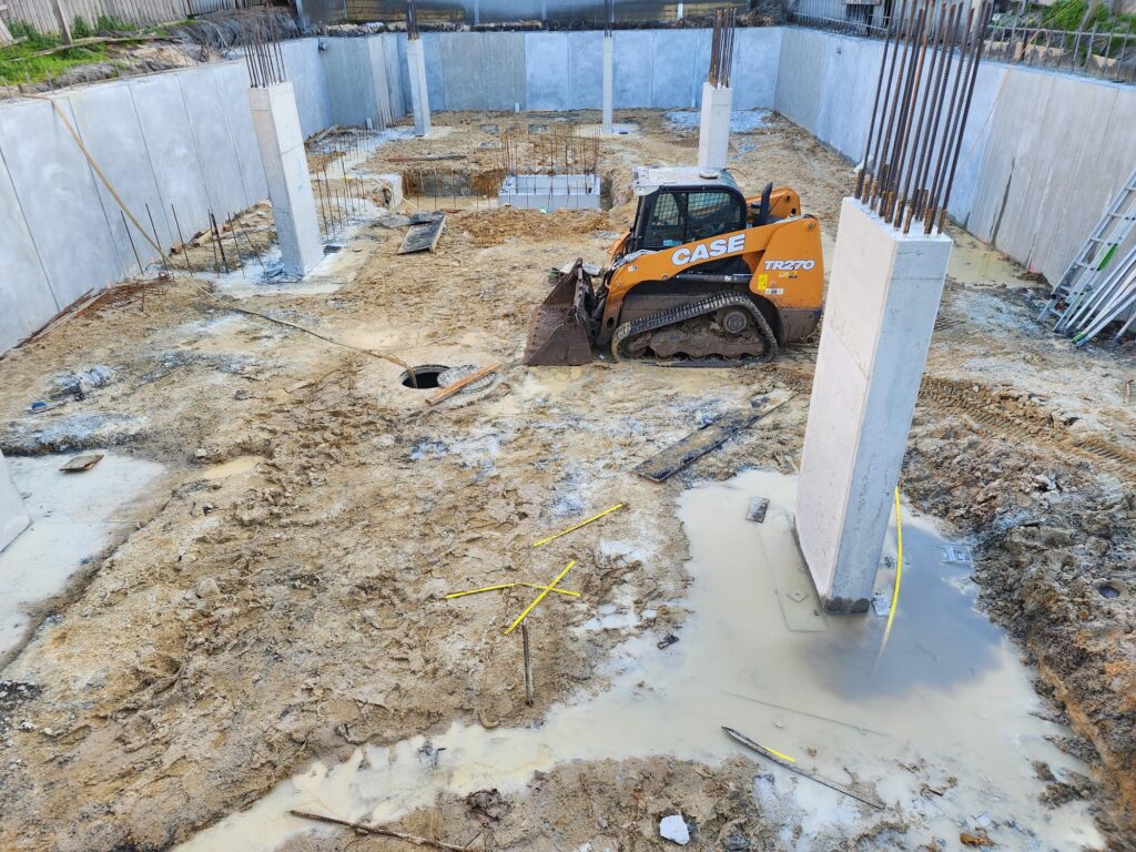 Compact track loader inside a basement dig with concrete walls and columns